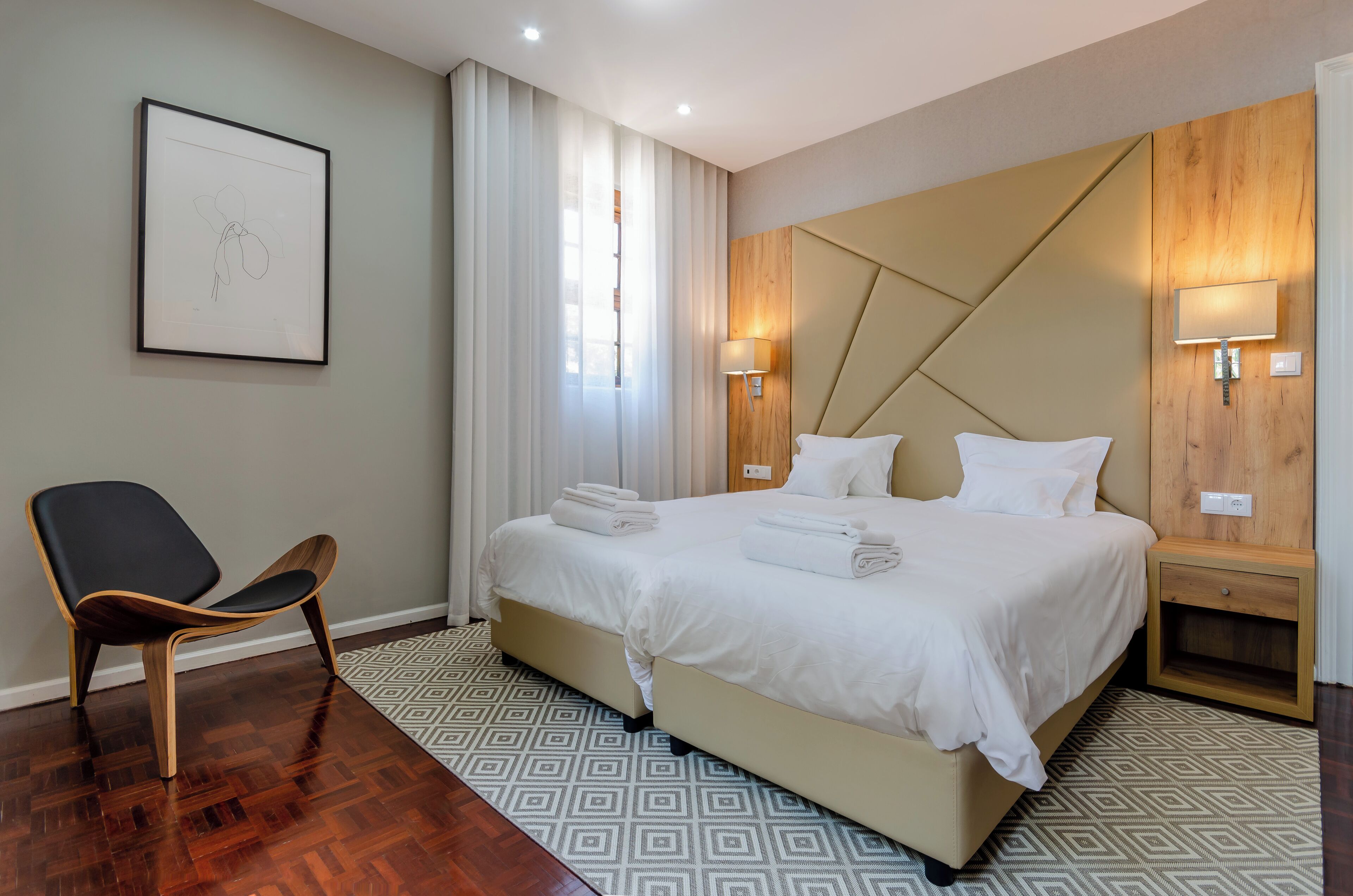 Ein modernes Hotelzimmer mit einem großen Bett, einem Sessel und einem gerahmten Kunstwerk an der Wand.