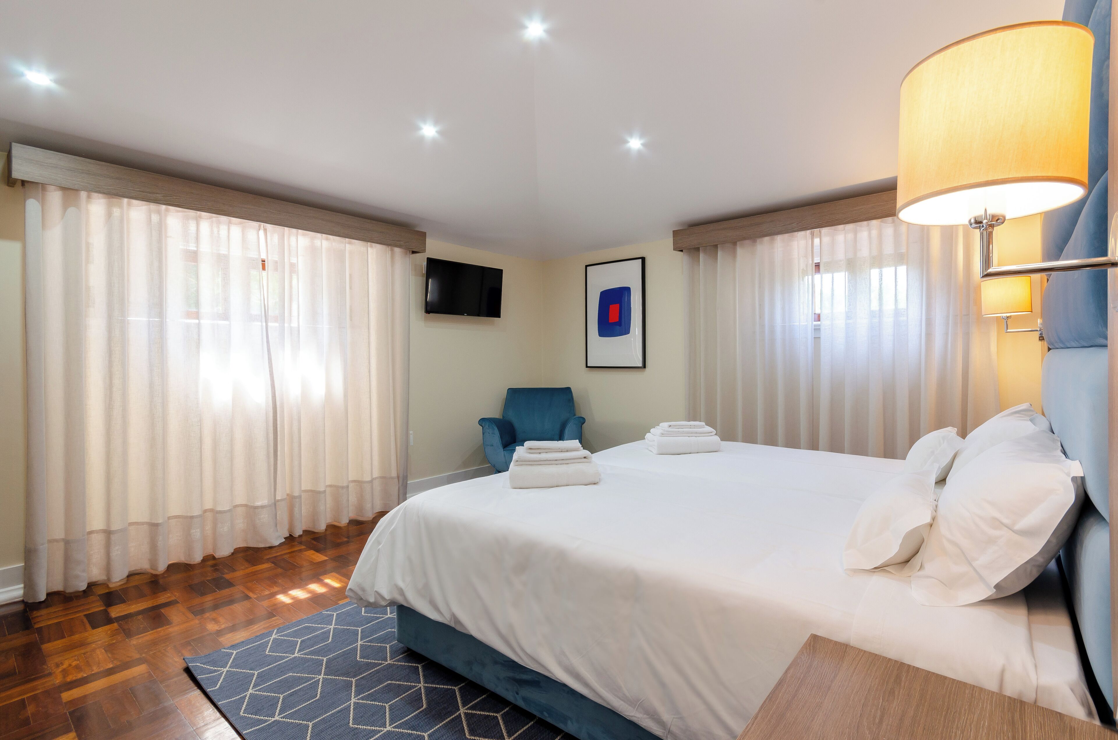 Een hotelkamer met een groot bed, een blauwe fauteuil, een flatscreen televisie en een wandlamp.