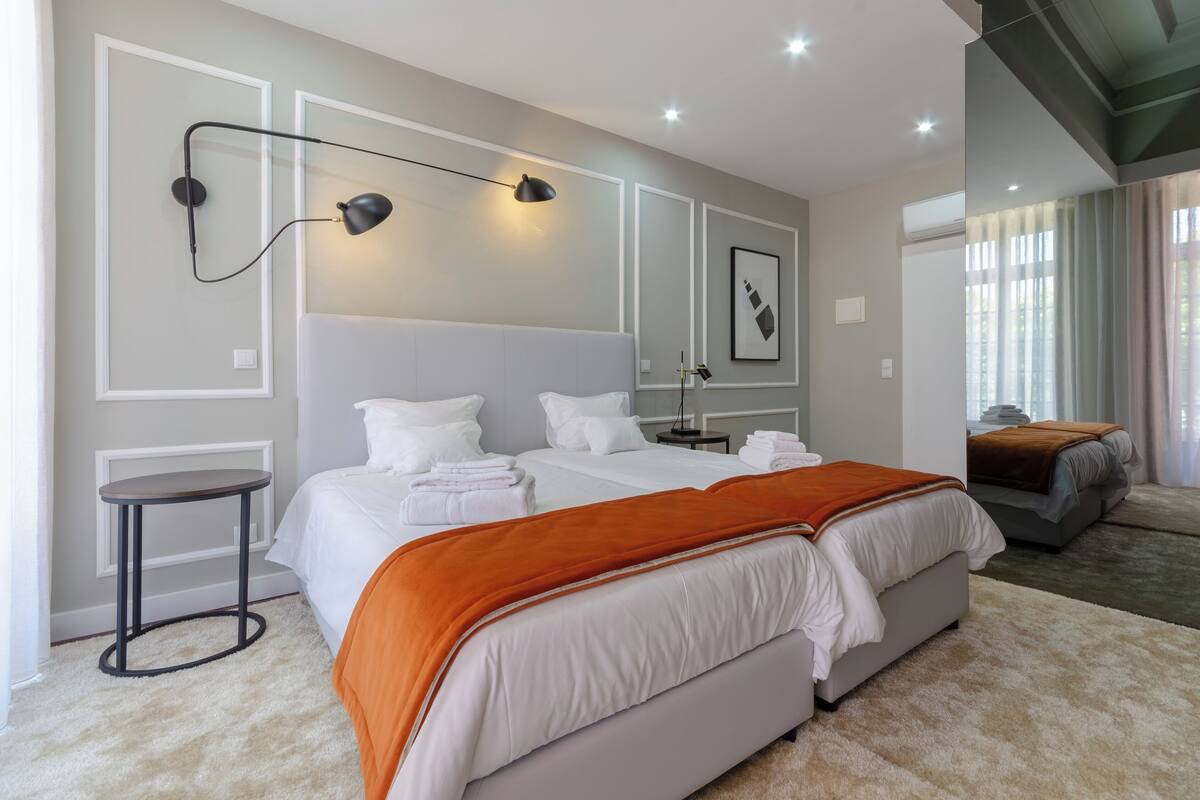 A modern bedroom with a large bed, a bedside table, a standing lamp, and a mirror on the wall.