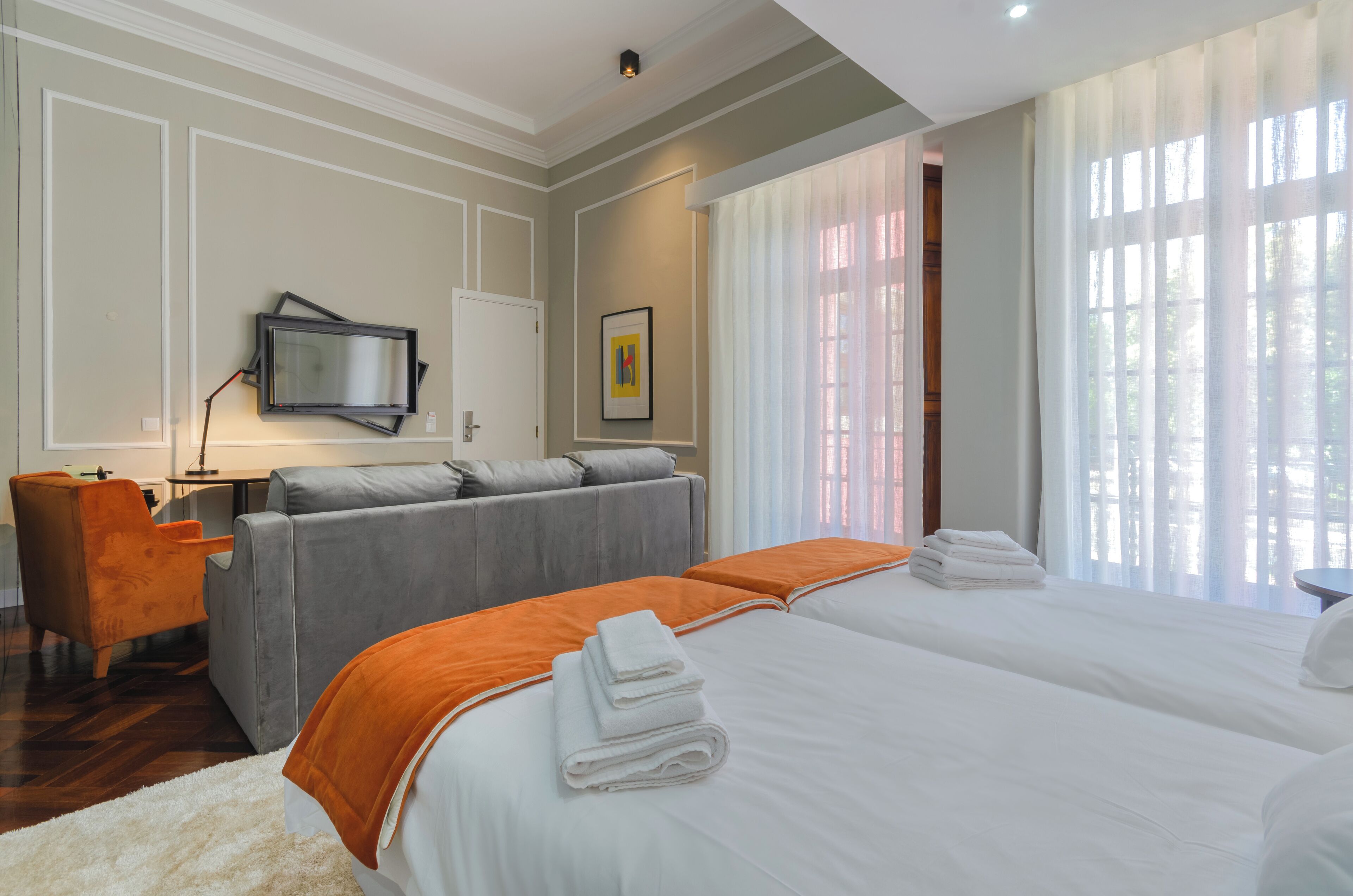 Une chambre d’hôtel avec un grand lit, un canapé, un bureau avec une chaise, une télévision et une fenêtre avec des rideaux.