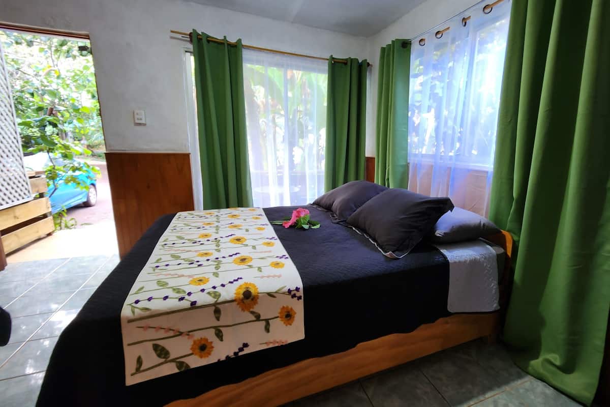 A bedroom with a bed, green curtains, and a view of the outdoors.