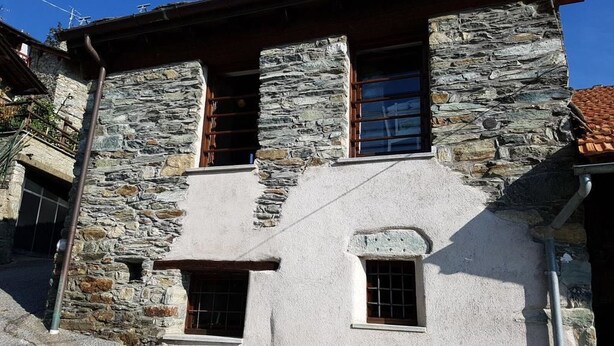 A stone building with a sloped roof, two windows, and a small door.