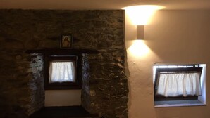 A stone fireplace with a framed picture above it, a lit wall sconce, and a window with curtains.