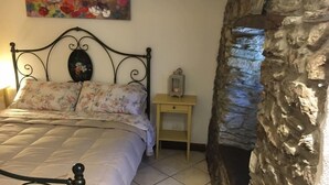 A bed with a floral duvet, a nightstand with a lantern, and a stone wall.