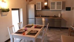 A modern kitchen with white cabinets, a stainless steel refrigerator, and a dining area with a white table and chairs.