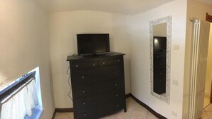 A corner room with a black dresser, a television on top, and a mirror on the wall.