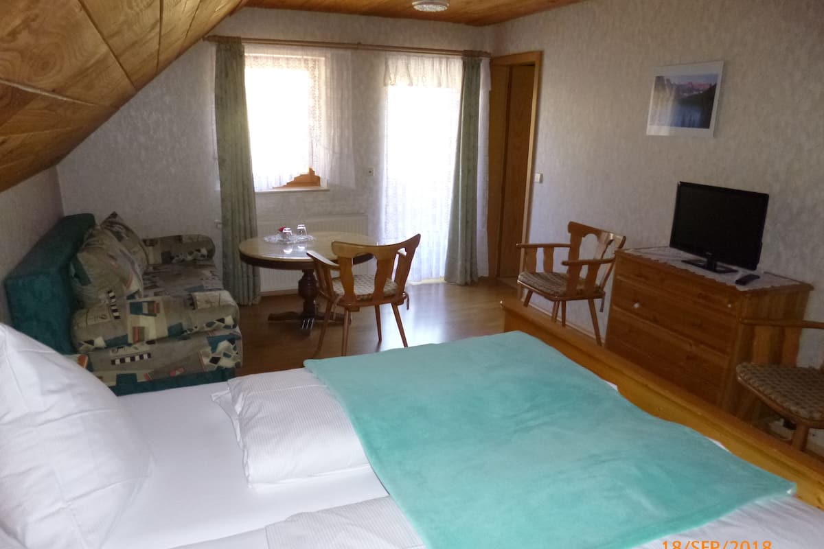A cozy room with a bed, a small table with chairs, a television, and a window with curtains.