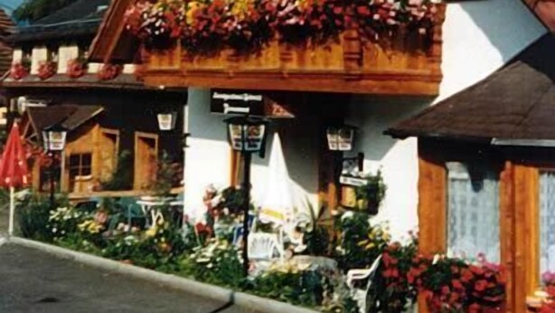 A traditional chalet-style building with a sloped roof and wooden balcony adorned with flowers. - Landgasthaus Gemsennest (Feldberg)