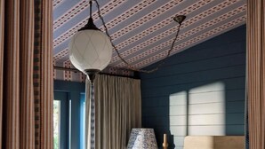 A bedroom with a bed, curtains, a lamp, and a patterned ceiling. - Cottages at Little Saint (Healdsburg)