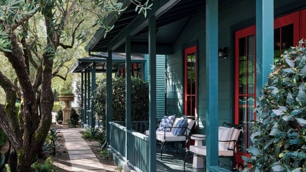 A covered porch with outdoor seating, surrounded by greenery and trees. - Cottages at Little Saint (Healdsburg)