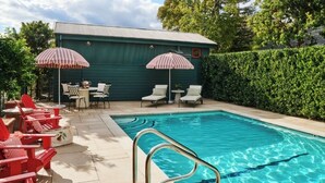 A swimming pool with a metal ladder, red lounge chairs, and two striped umbrellas. - Cottages at Little Saint (Healdsburg)