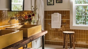 A bathroom with a large mirror, two sinks, a towel rack, a shower area, and framed artwork on the wall. - Cottages at Little Saint (Healdsburg)