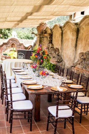 An outdoor dining area with a long table set for a meal, surrounded by wooden chairs. - Hotel La Casona de Antigua (Antigua Guatemala)