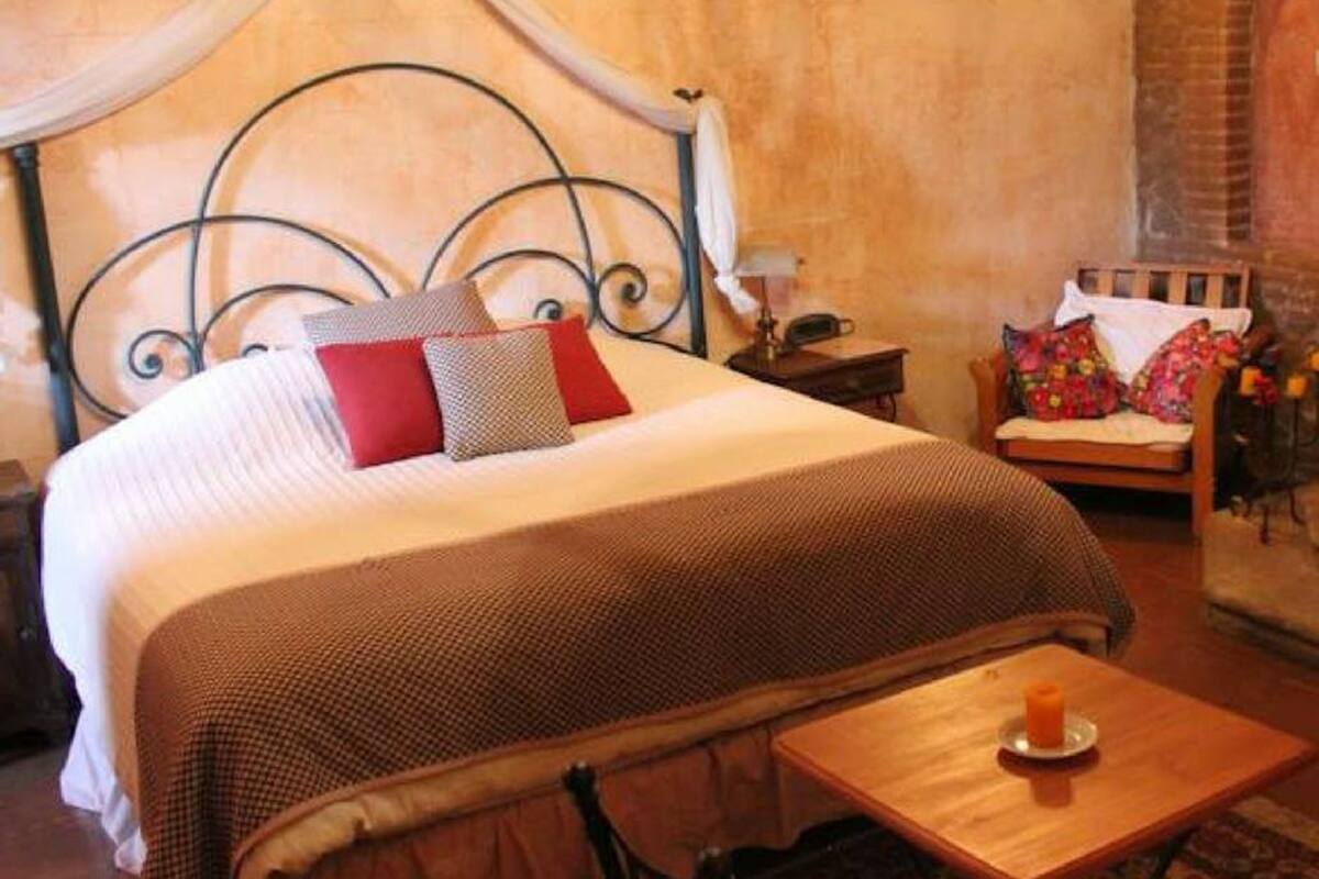 Ein Schlafzimmer mit einem Himmelbett, einem kleinen Holztisch mit Kerze und einem Sessel mit farbenfroher Sitzkissen.