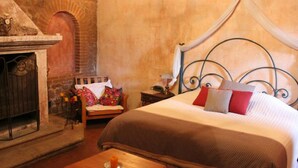 A bedroom with a stone fireplace, a bed with a metal headboard, and a small bedside table. - Hotel La Casona de Antigua (Antigua Guatemala)