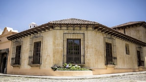 A building with a tiled roof, large windows with iron bars, and a small garden area with flowers. - Hotel La Casona de Antigua (Antigua Guatemala)