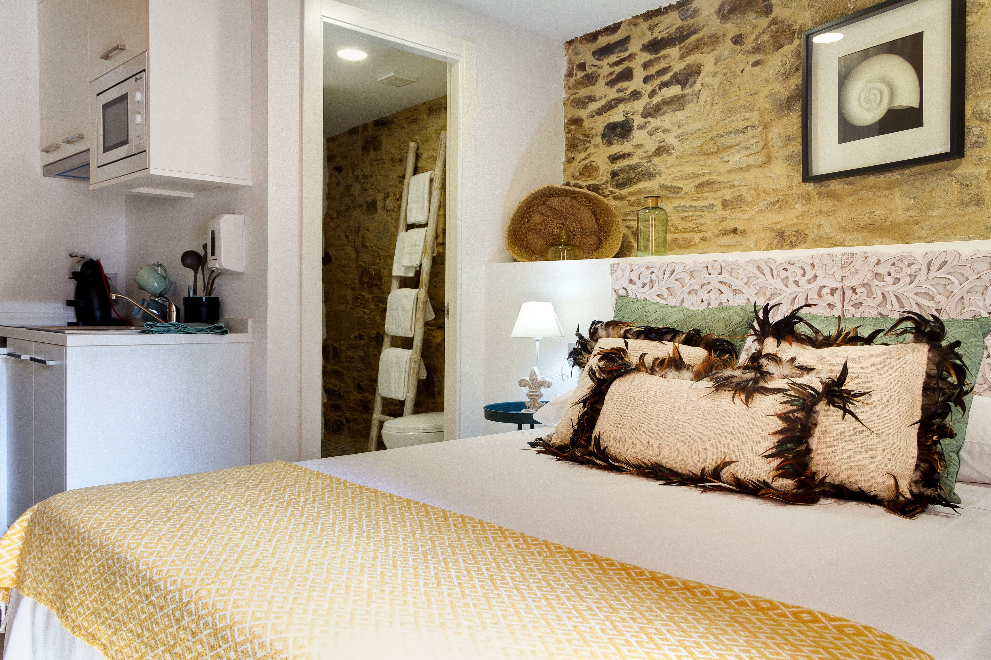 A bedroom with a bed, a dresser, a microwave, and a stone wall.