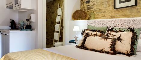 A bedroom with a bed, a dresser, a microwave, and a stone wall.