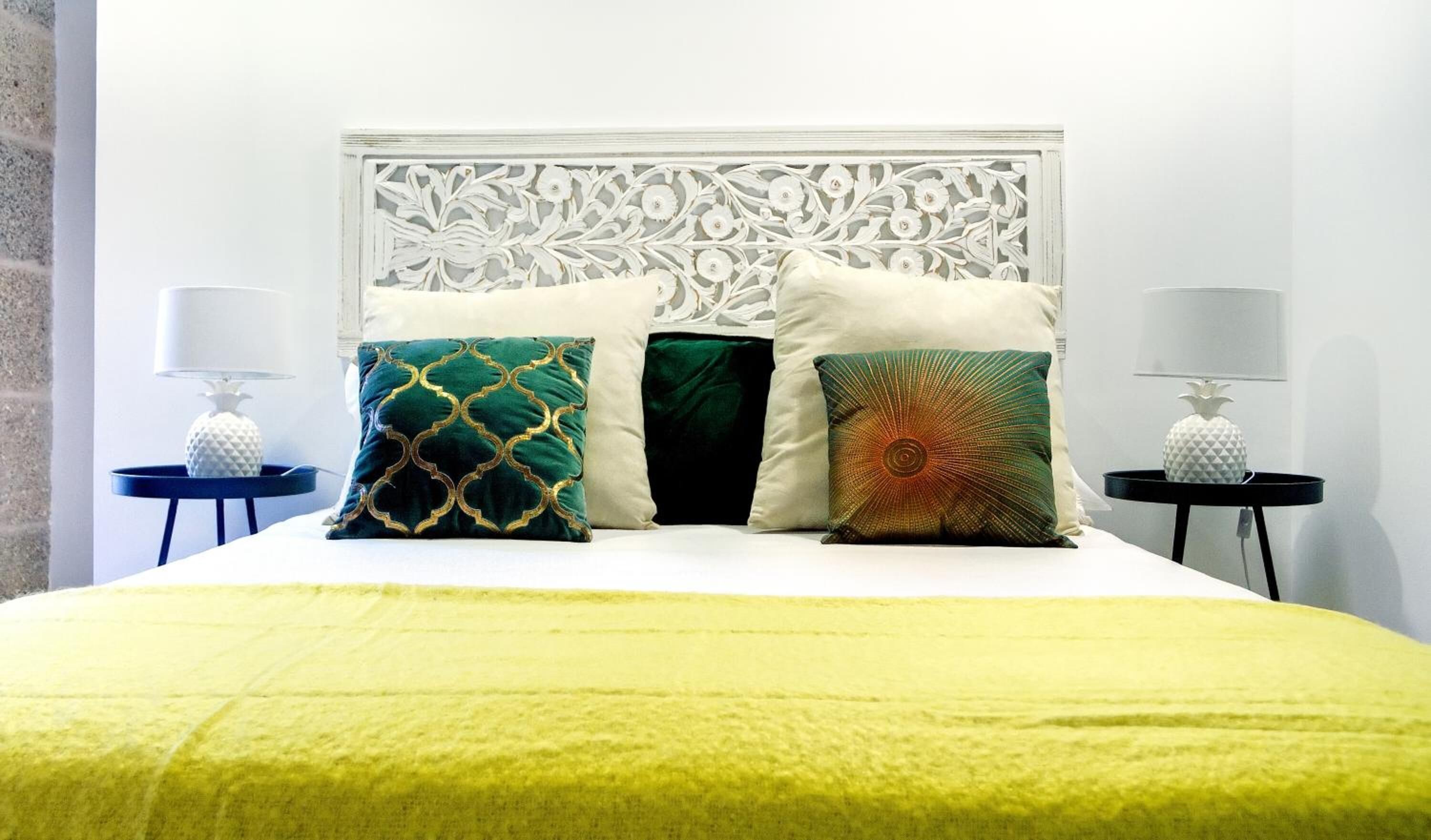 A bed with a white headboard, a yellow bedspread, and four decorative pillows. There are two nightstands with lamps on either side of the bed.