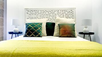 A bed with a white headboard, a yellow bedspread, and four decorative pillows. There are two nightstands with lamps on either side of the bed.