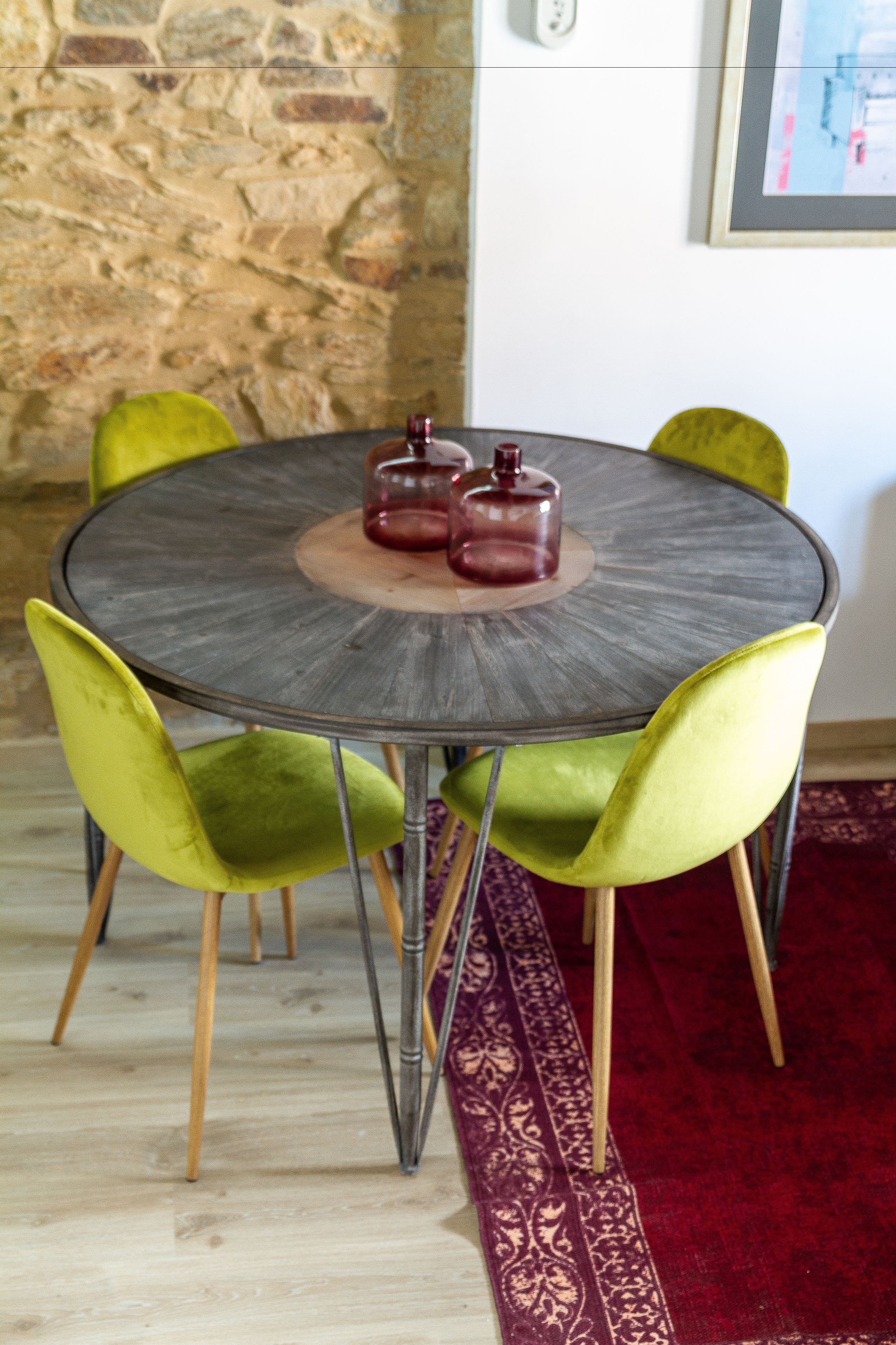 A round table with four chairs, a red rug, and a stone wall in the background.