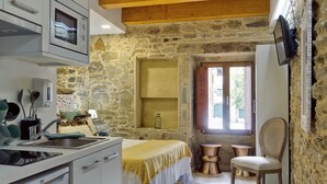 A rustic kitchen with a stone wall, wooden ceiling, and a bed with a yellow blanket. - Rúa Travesa (Santiago de Compostela)