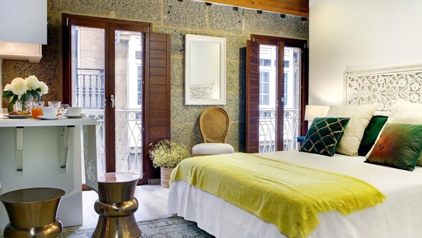 A bedroom with a bed, a bedside table, a chair, and a window. - Rúa Travesa (Santiago de Compostela)