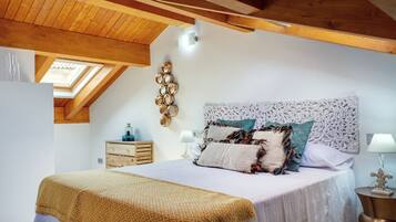 A bedroom with a wooden ceiling, a skylight, a bed with patterned bedding, a bedside table with a lamp, and a wall-mounted mirror.