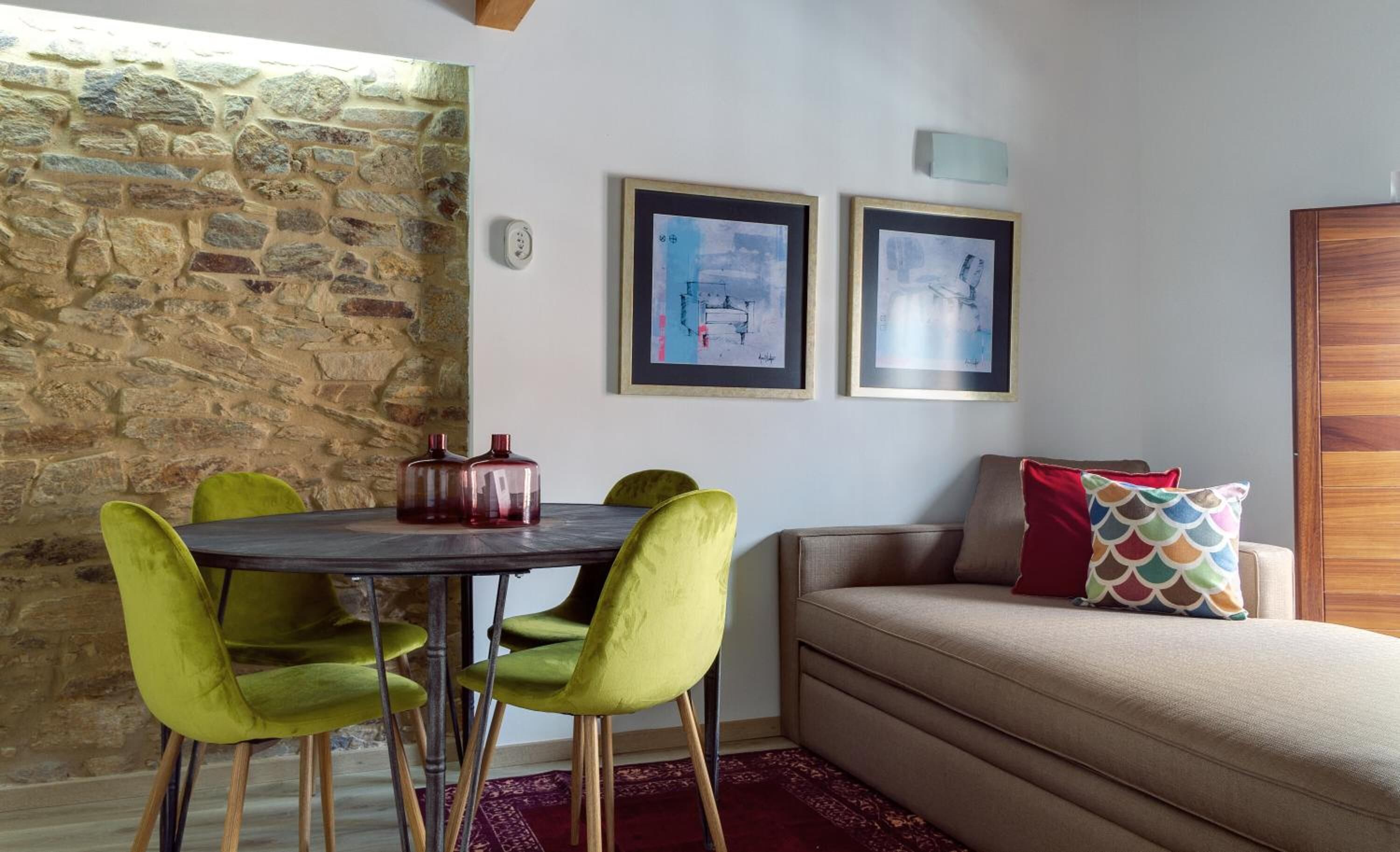 Una habitación acogedora con pared de piedra, una mesa de comedor con sillas, un sofá y dos cuadros enmarcados en la pared.