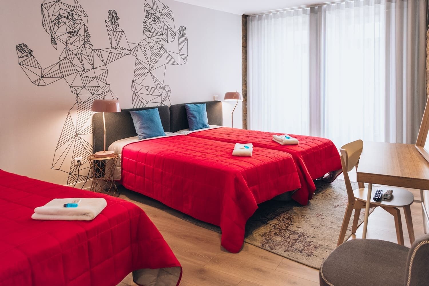 A hotel room with two beds, a desk, and a chair. There is a wall art piece above the beds.