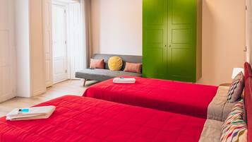 Habitación de hotel con dos camas, un armario verde, un sofá gris y una ventana con cortinas.