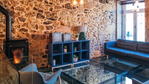 A cozy living room with a stone wall, a fireplace, a blue sofa, and a glass coffee table. - In Barcelos Hostel & Guest House (Barcelos)