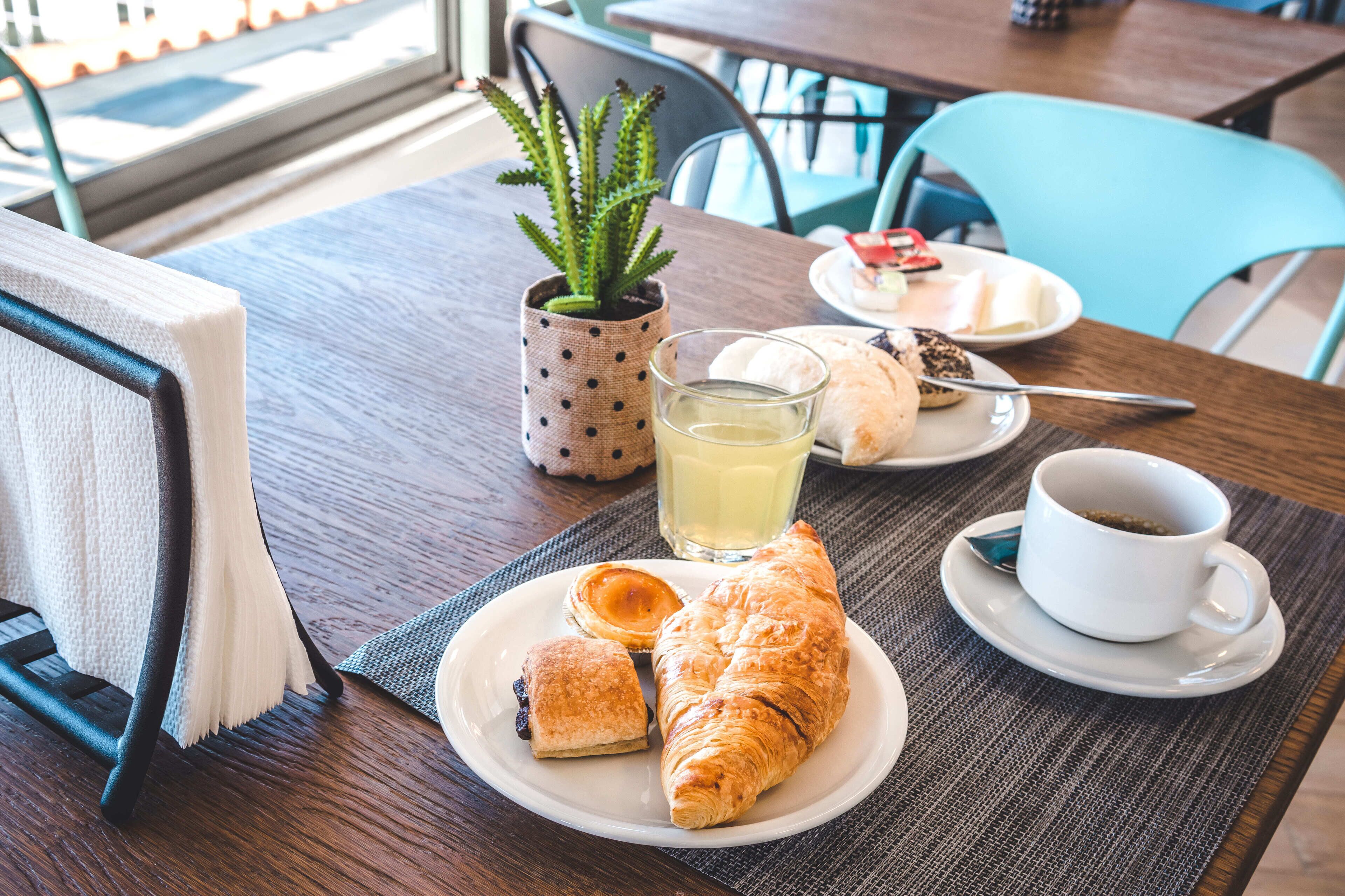 A breakfast setting with croissants, a glass of juice, and a cup of coffee on a table.