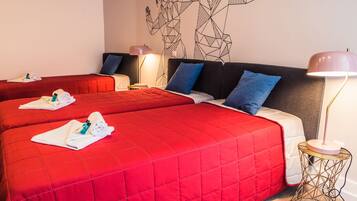 Habitación de hotel con dos camas, cada una con una colcha acolchada roja y toallas. Hay una obra de arte en la pared sobre las camas y una lámpara en una mesita de noche.