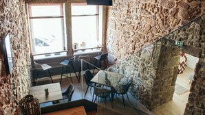 A modern interior with stone walls, a staircase, and a dining area with tables and chairs. - In Barcelos Hostel & Guest House (Barcelos)