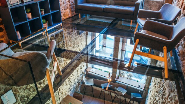 A modern interior with a glass floor, seating area, and a stone wall backdrop. - In Barcelos Hostel & Guest House (Barcelos)