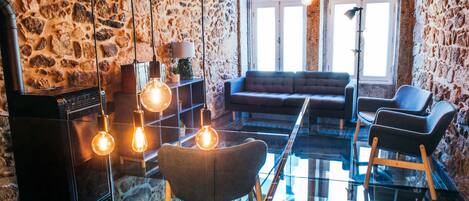 Uma sala de estar moderna com parede de pedra, uma mesa de centro de vidro, um sofá e duas poltronas.