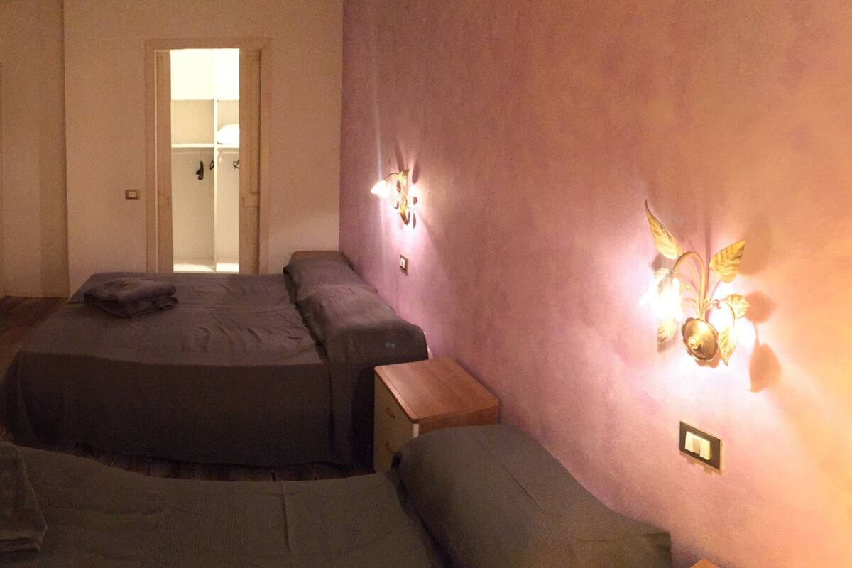 A small, dimly lit room with a bed, a sofa, and a wooden desk.