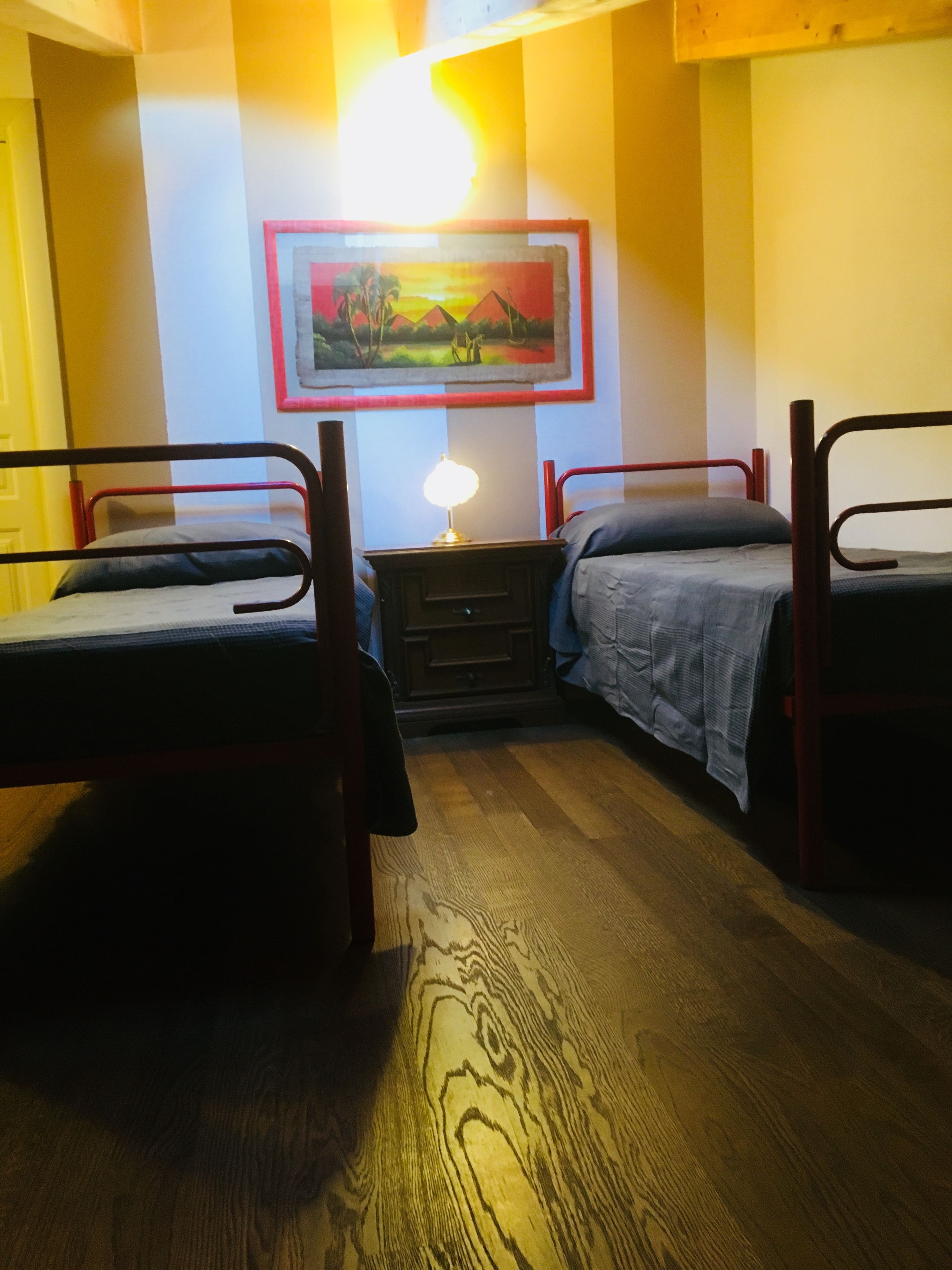 Een kamer met twee eenpersoonsbedden, een nachtkastje met een lamp en een lijst met een afbeelding aan de muur.