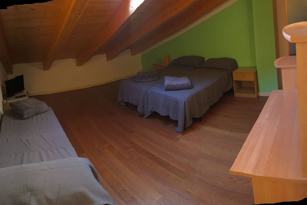 A bedroom with two beds, wooden flooring, and a sloped ceiling.