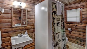 A wooden cabin bathroom with a sink, mirror, and shower. - Rib Waters Inn (Rib Lake)