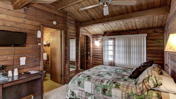 A log cabin bedroom with a bed, a desk, a ceiling fan, and a television on the wall. - Rib Waters Inn (Rib Lake)