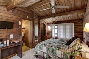 A log cabin bedroom with a bed, a desk, a ceiling fan, and a television on the wall. - Rib Waters Inn (Rib Lake)