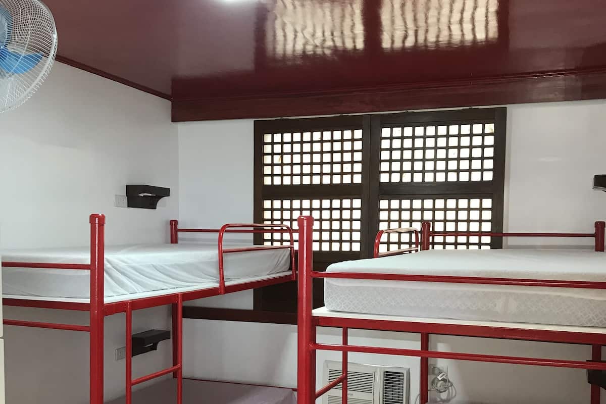 Ein Schlafsaalzimmer mit Etagenbetten, einem Deckenventilator und einem Fenster mit Gittermuster.