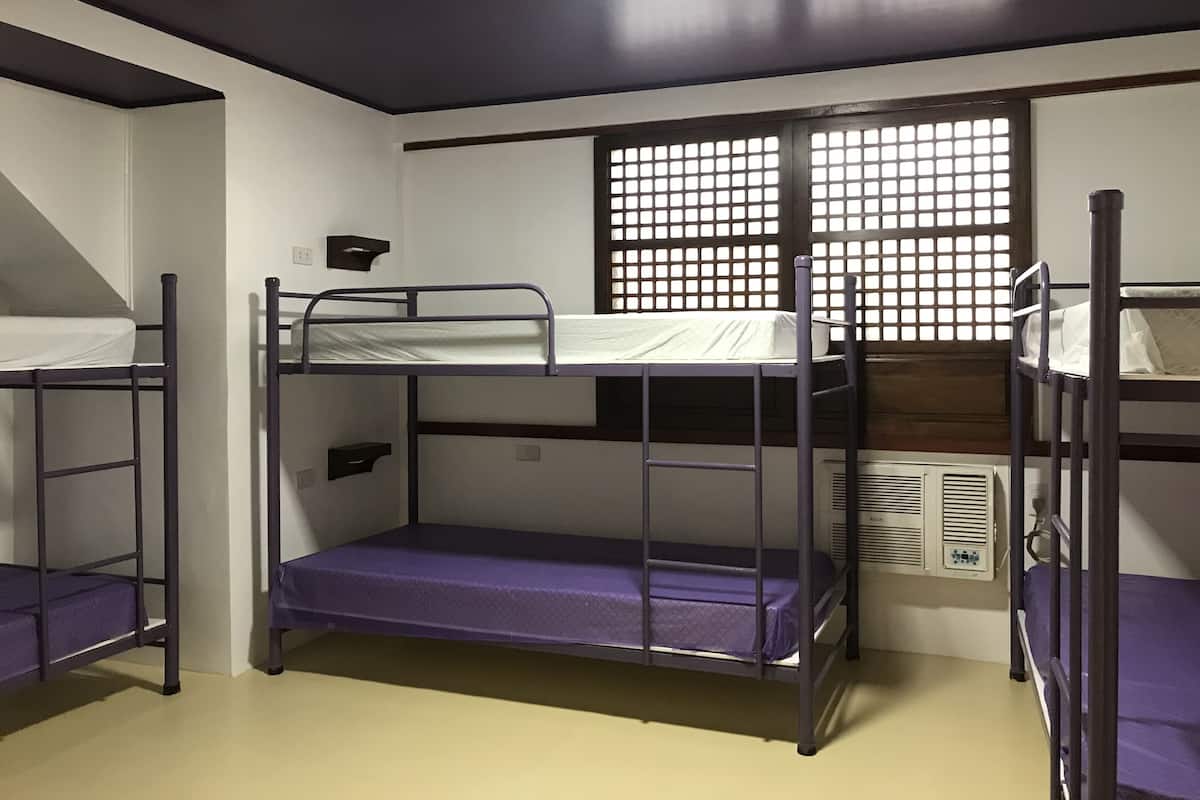 Ein Schlafsaalzimmer mit Stockbetten, einem Fenster mit Gittermuster und einem Wandheizgerät.