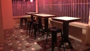 Een restaurantinterieur met meerdere tafels en krukken, vloer met patroon en decoratieve metalen roede voor de ramen.