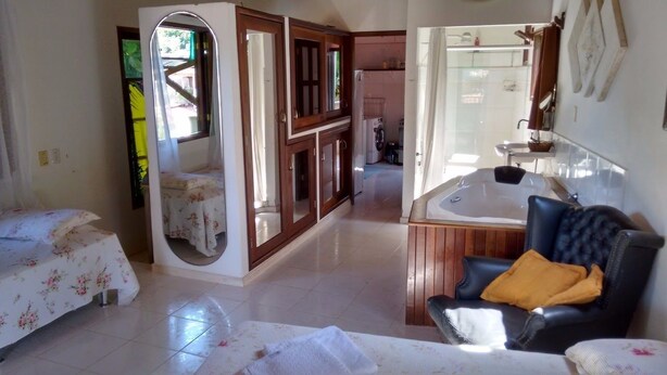 Un dormitorio con cama, una silla, un baño con lavamanos y espejo, y una zona de cocina.