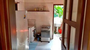 Cocina compacta con refrigerador, lavadora y horno pequeño. Encima del horno, hay un estante con frascos y recipientes.