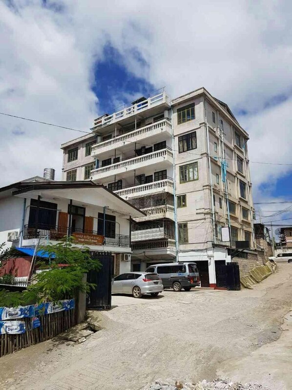 A multi-story building with balconies, a parking area, and a gated entrance.