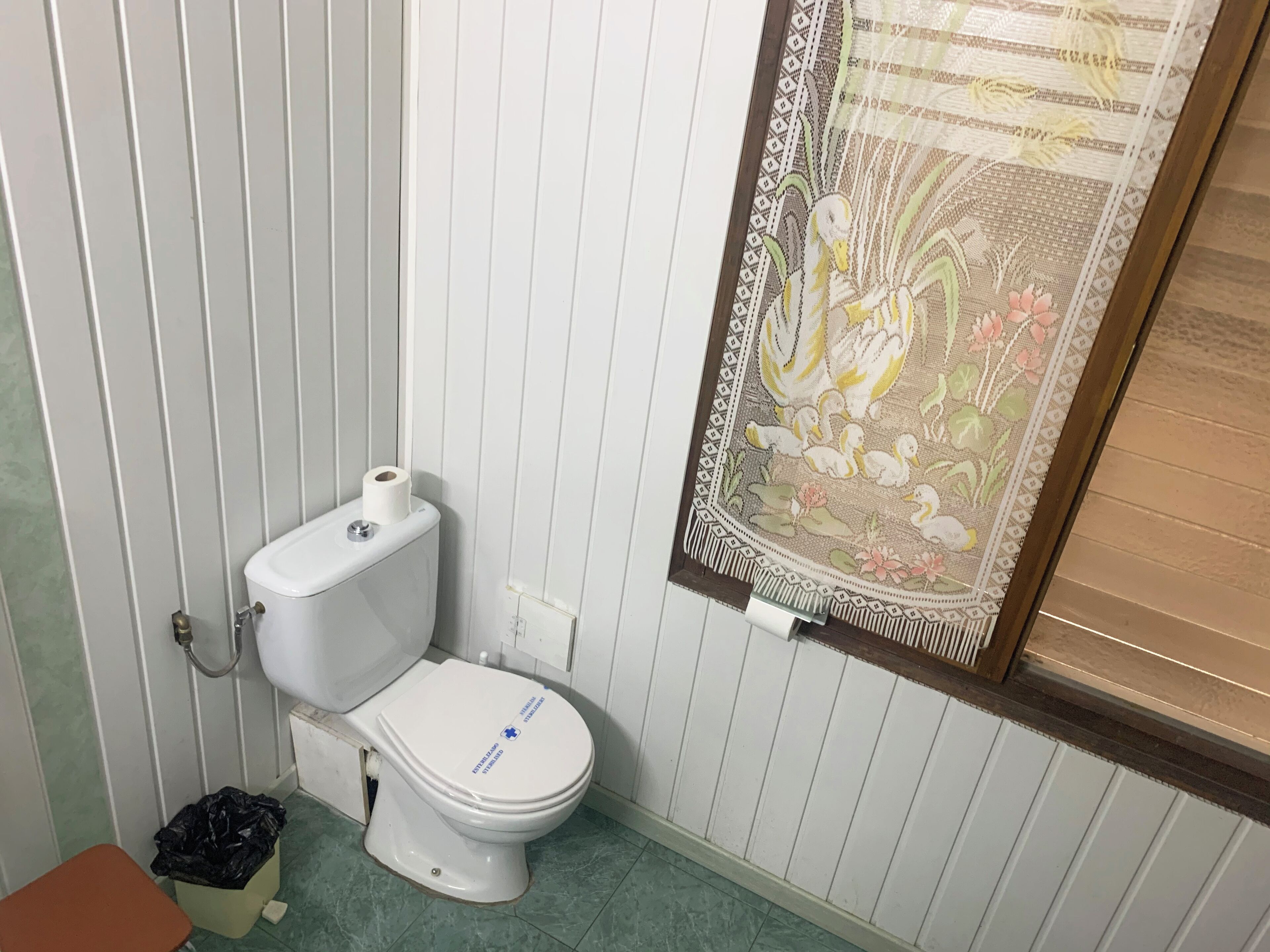 Un baño con inodoro, un bote de basura y una cortina decorativa.